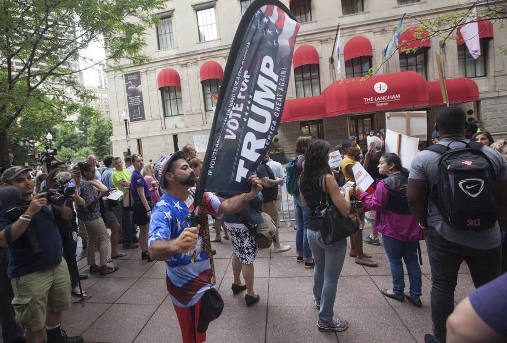 A Trump supporter walks through the protesters carrying a "Vote for Trump" banner. (Joe Difazio for WBUR)