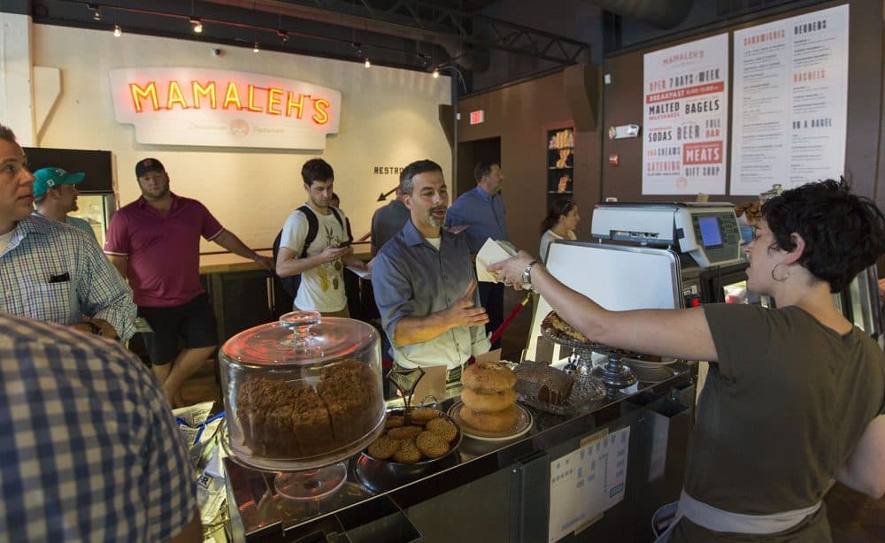 Mamaleh's co-owner Rachel Miller Munzer passes a sandwich over the take out counter to a customer. (Jesse Costa/WBUR)