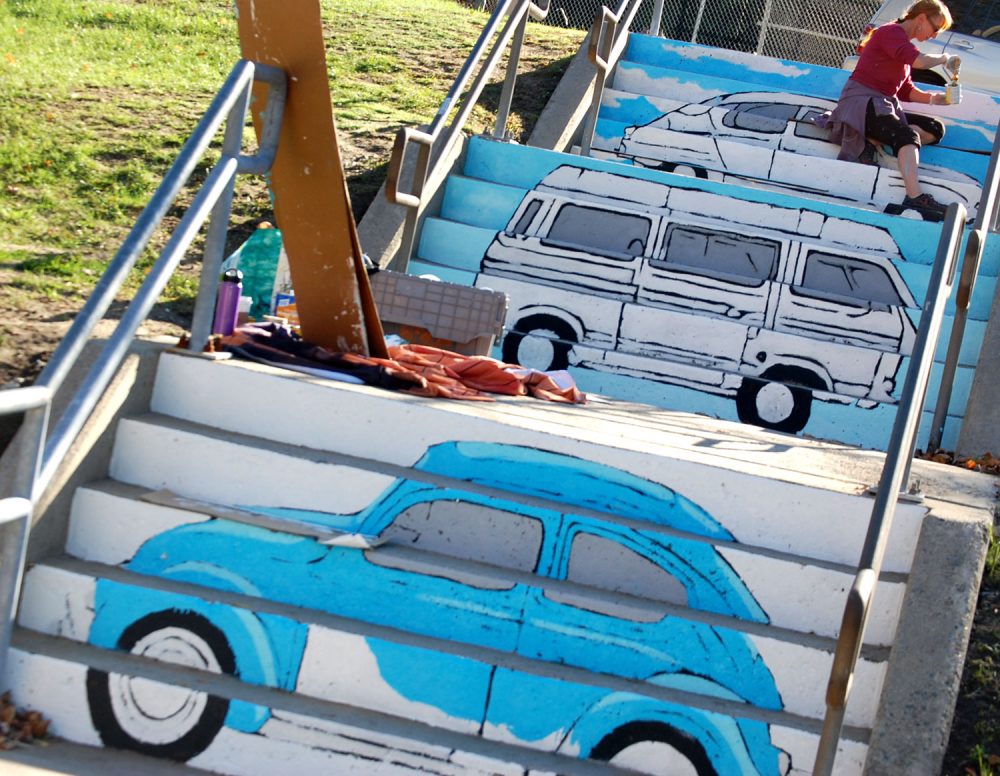 Liz LaManche paints “The Soul’s Journey as a Series of Weird Old Automobiles" in the park at the intersection of Pearl and Medford streets in Somerville. (Greg Cook)
