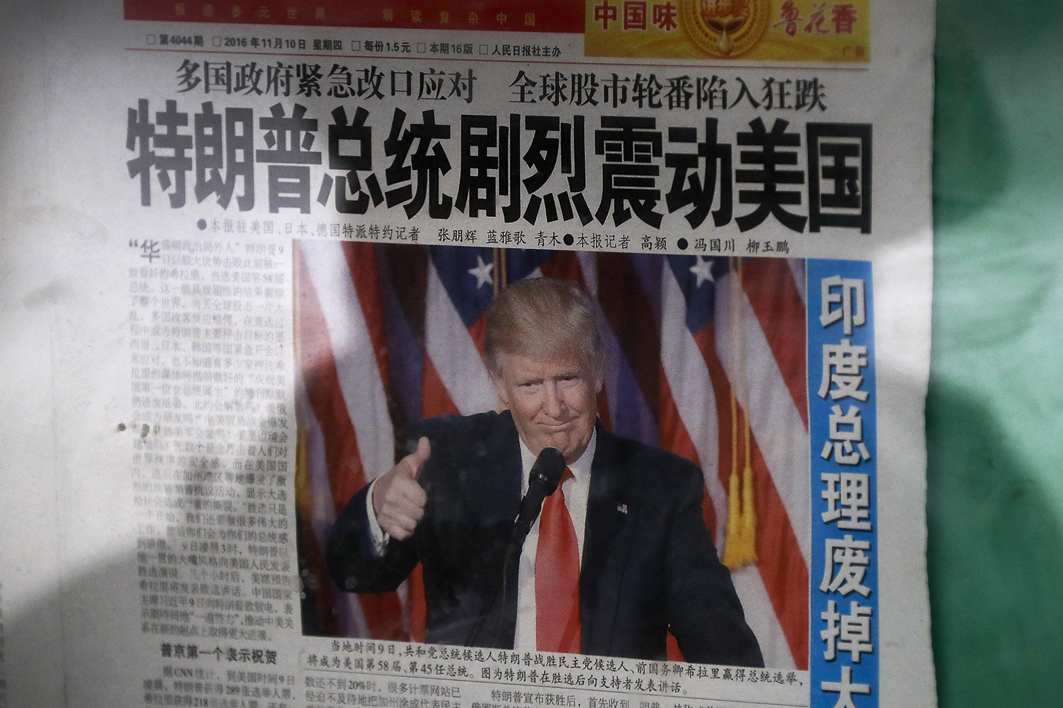 A man is reflected on a glass as he reads a Chinese newspaper with a photo of U.S. President-elect Donald Trump, displayed on a newspaper board in Beijing. The headline reads "President Donald Trump delivers a mighty shock to America." (Andy Wong/AP)