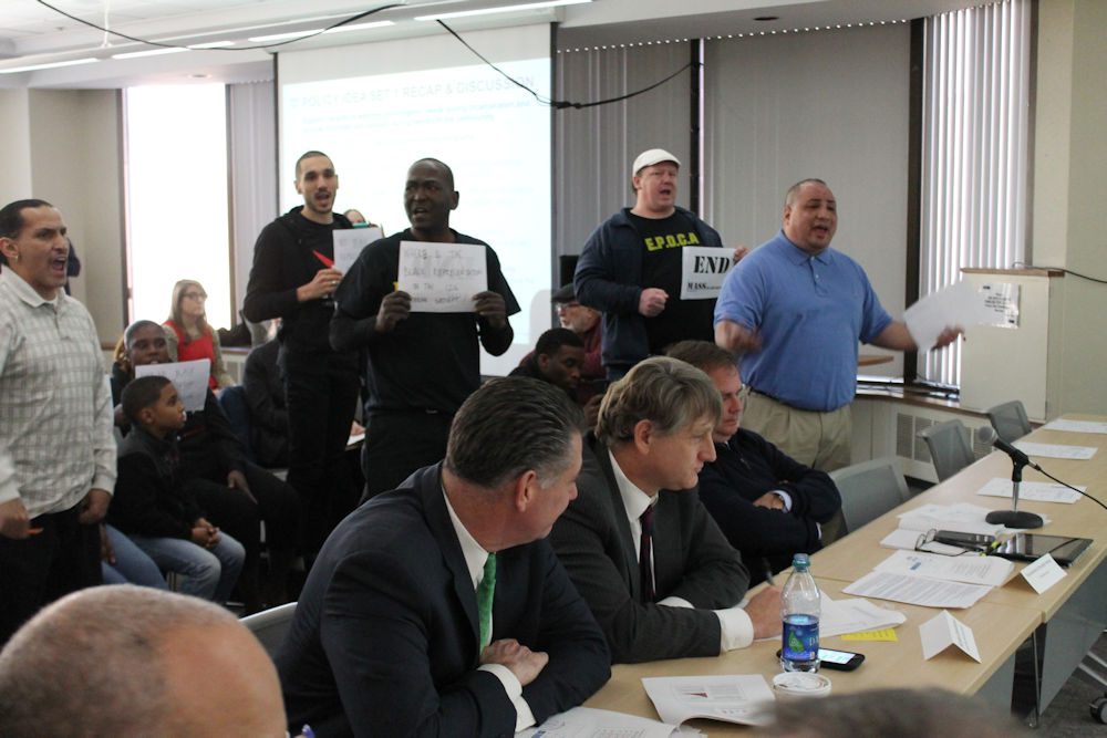 Calvin Feliciano (far right), deputy political director for SEIU 509, interrupted Wednesday's meeting of a criminal justice working group to express the need for sentencing reforms and led protesters in a "Jobs not Jails" chant. (Antonio Caban/SHNS)