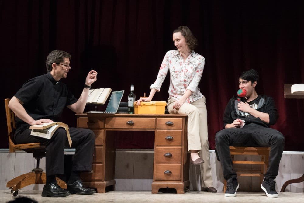Margery (played by Marianna Bassham) sits on the desk speaking with Pastor Greg (played by Lewis D. Wheeler). (Courtesy Glenn Perry Photography/Speakeasy Stage Company)