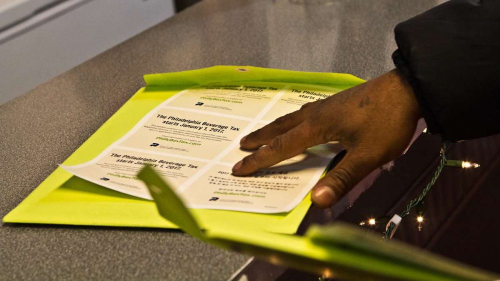Thomas Walker, a member of the city’s Soda Tax Street Team, passes off a packet of information to employees of a corner store in South Philadelphia. (Kimberly Paynter/WHYY)