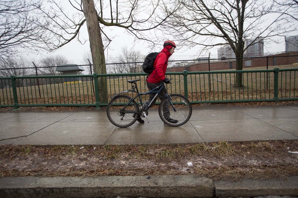 A cyclist walks his bike as he struggles to maneuver on the icy sidewalk of Memorial Drive in Cambridge. (Jesse Costa/WBUR)