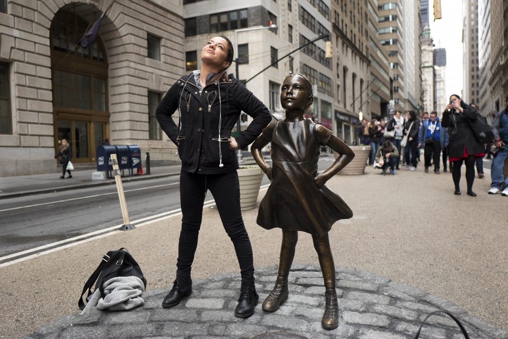 A woman strikes a pose with the "Fearless Girl" statue on Wednesday, International Women's Day. (Mark Lennihan/AP)