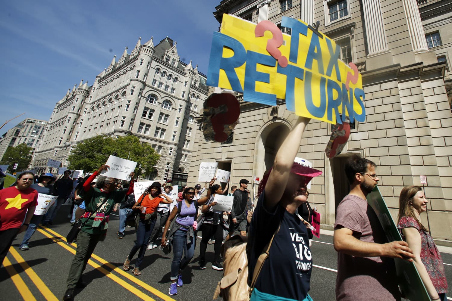 Protesters march past the Trump International Hotel, backround left, and the Internal Revenue Services building, right, during a Tax Day demonstration in Washington, Saturday, April 15, 2017, calling on President Donald Trump to release his tax returns. (Manuel Balce Ceneta/AP)