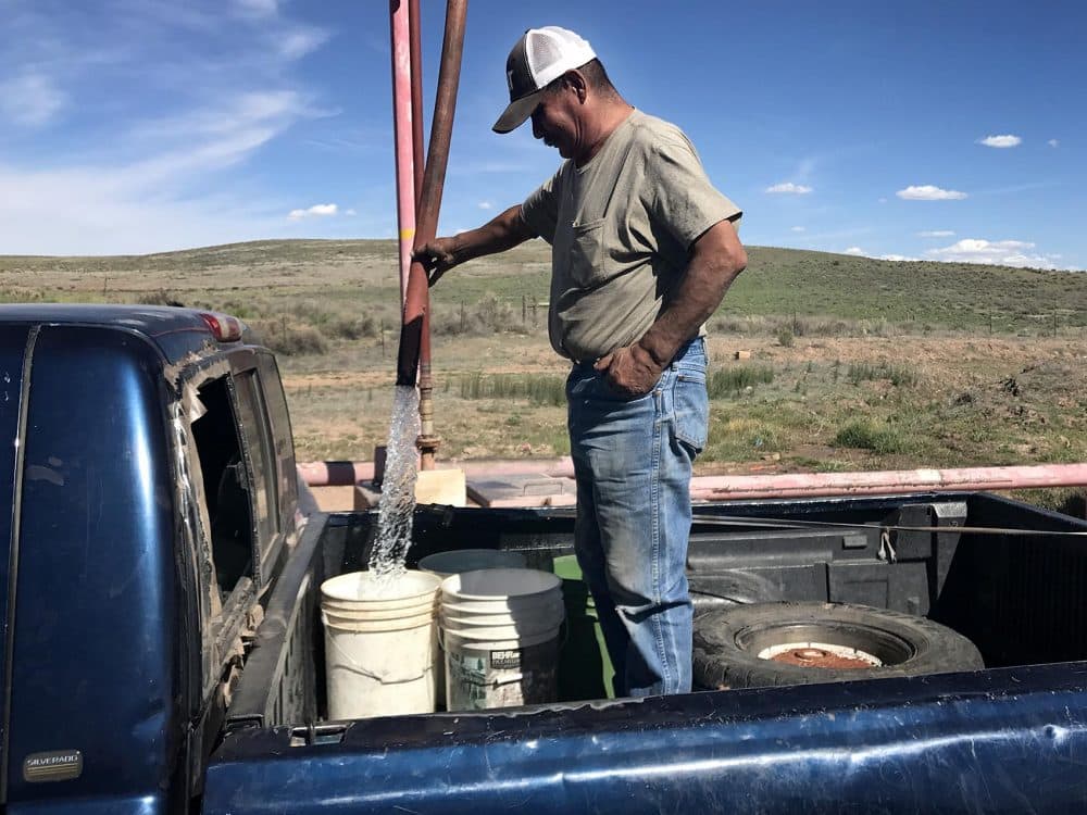 John Davis fills water buckets in the back of his truck at a well at the Kayenta coal mine, where locals come to get water for their homes. (Peter O'Dowd/Here & Now)