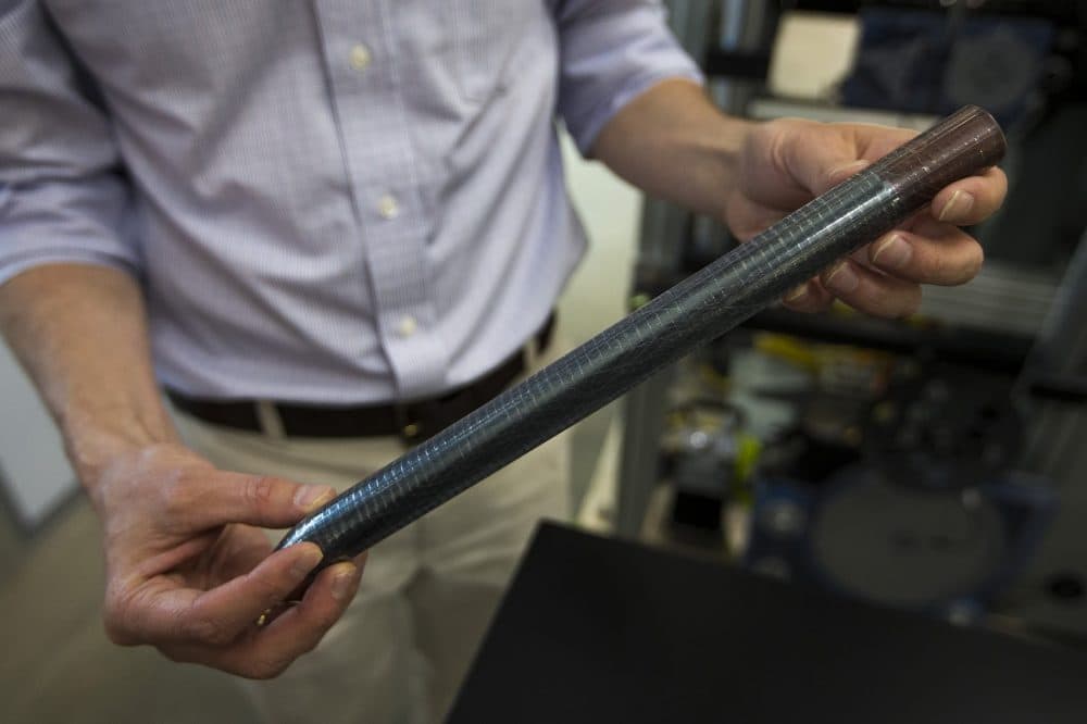 Sasha Stolyarov holds a "preform," which is the starting material where devices are integrated. Functionality is created at this level by introducing semiconducors and metals to the "preform" which is then drawn or pulled into fibers. (Jesse Costa/WBUR)