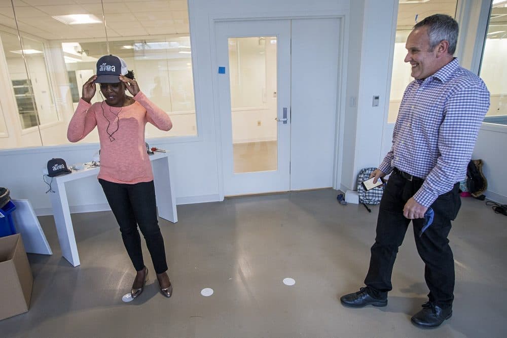 WBUR reporter Zeninjor Enwemeka tries on an AFFOA trucker hat which serves as an optical receiver working with LED lights installed above it. The hat has an audio plug to attach earbuds to listen to the sound that the hat's fabric is streaming from the lights. (Jesse Costa/WBUR)