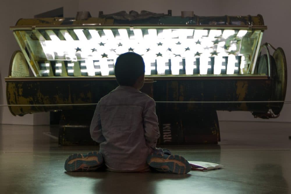 Nine-year-old Danny Zheng colors on the floor in front of Nari Ward's "Tanning Bed." (Jesse Costa/WBUR)