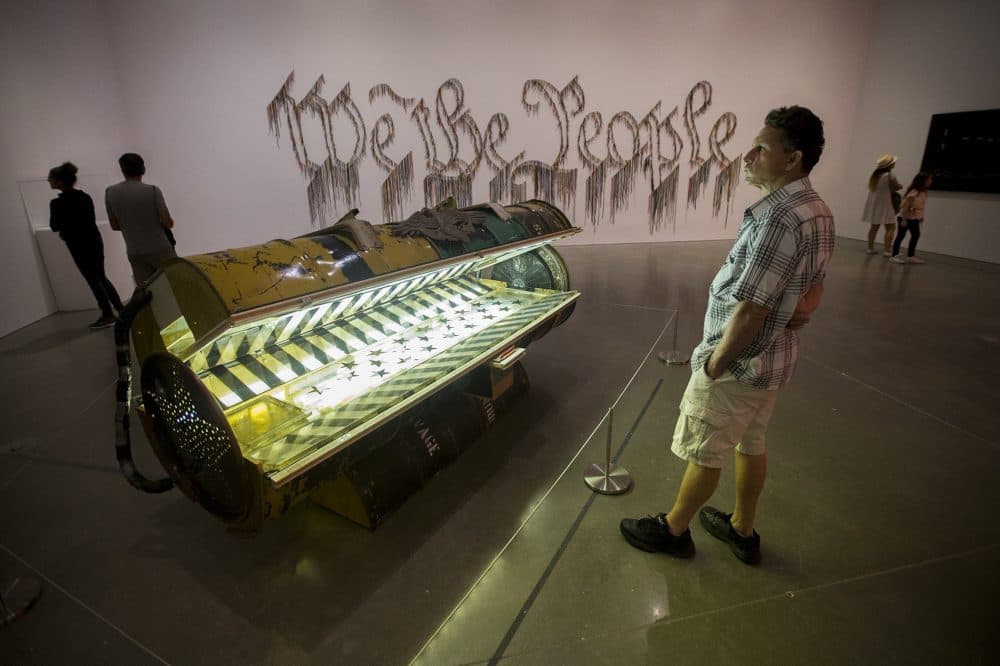 A museum patron looks at Nari Ward's "Tanning Bed." The work, "We The People," is seen in the background. (Jesse Costa/WBUR)