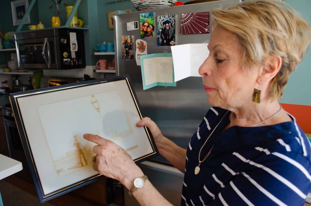 East Boston resident Michele Modica shows a framed picture of her family standing on the shore behind her childhood home at a time when her family could clearly see an undeveloped Boston skyline from their property. (Elizabeth Gillis/WBUR)