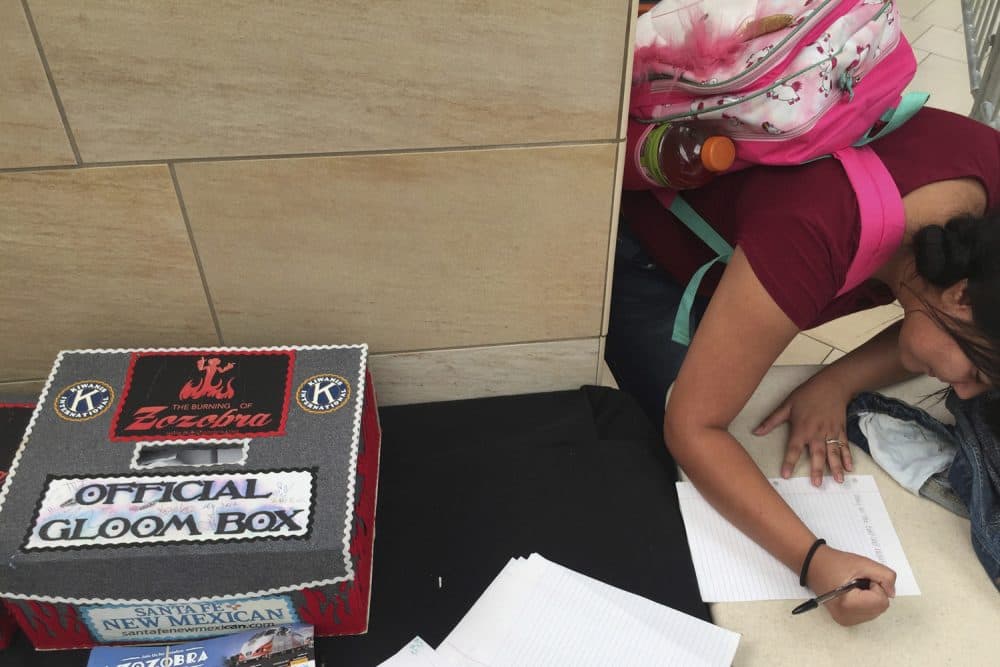 A high school student writes a note in August 2017 about recent worries that will be stuffed into a giant marionette to be burned away at the Zozobra festival in New Mexico. (Morgan Lee/AP)