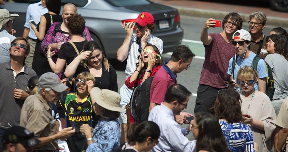 On the sidewalk in front of the Boston Public Library, people share protective glasses so they can look up to see the solar eclipse. (Robin Lubbock/WBUR)