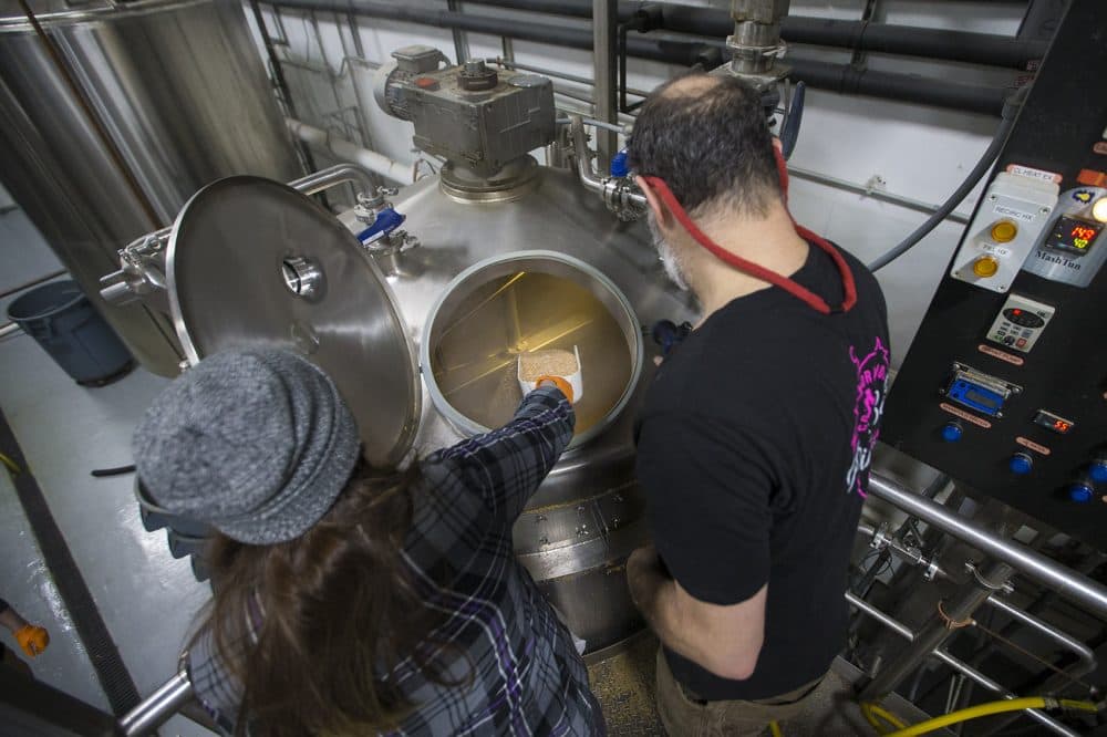 Matthew Steinberg watches as Katie Beaucage adds rice hulls to the wort in the mash tun. (Jesse Costa/WBUR)