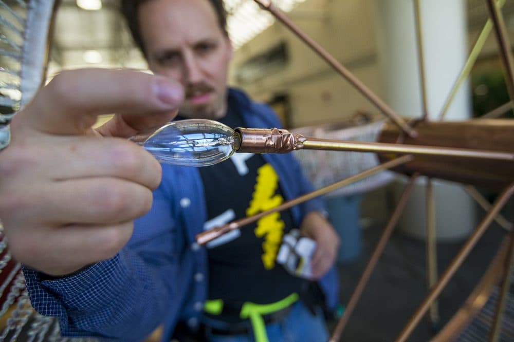 Taylor Hansen installs a light bulb onto one of the chandeliers. (Jesse Costa/WBUR)