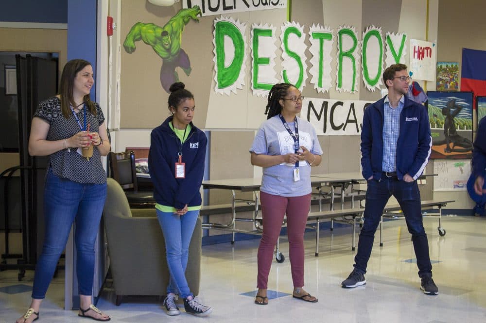 In front of a "Destroy MCAS" sign on the wall, from left, Megan Sanchez, Samantha Suarez, Pertreena Cherrie and Peter Perry-Friedman pause for a morning staff meeting at KIPP Academy Boston. (Carrie Jung/WBUR)