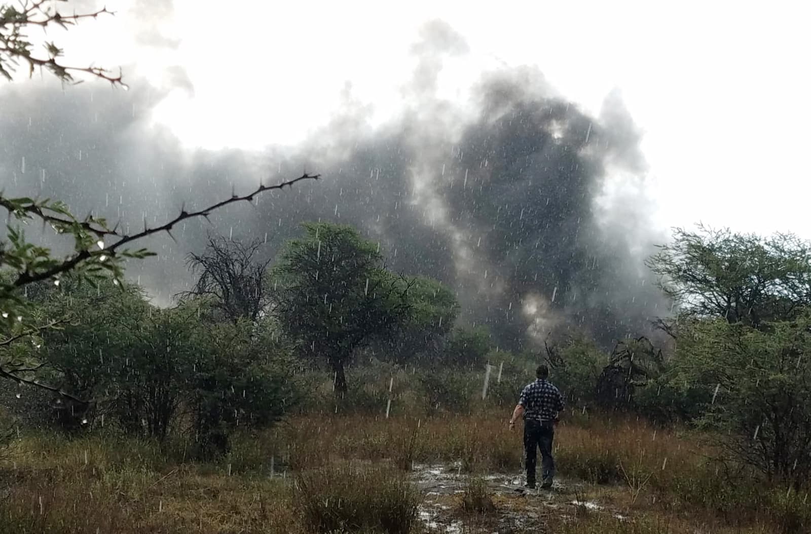 Alberto Herrera stands in a rain shower in a field watching smoke billow from the downed Aeromexico jetliner he was traveling in, near the airport in Durango, Mexico July 31, 2018. (Alberto Herrera via AP)