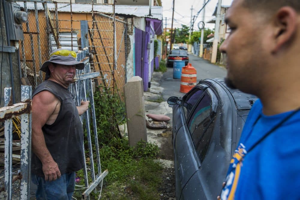 Angel Rosario, right, and Jose Contreras speak in front of Contreras' home as he takes a break from rebuilding it. (Jesse Costa/WBUR)