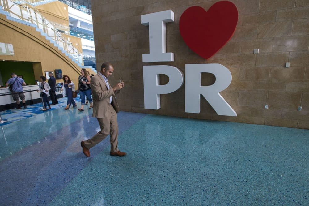 Economist and professor at the University of Puerto Rico Jose Caraballo-Cueto walks past a giant sign in the Puerto Rico Convention Center. (Jesse Costa/WBUR)