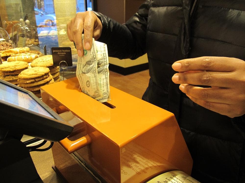 A customer inserts cash into a donation box to pay for her order at Panera Cares in Boston. (Kevin Sullivan/Here & Now)