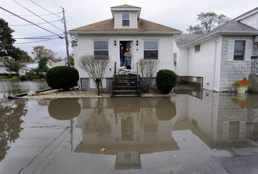 Anthony and Paula Bacco with their cat, Phoebe pose for a photogaph in their doorway barricaded with sand bags for protection against flooding from Hurricane Sandy. (Kathy Kmonicek/AP)