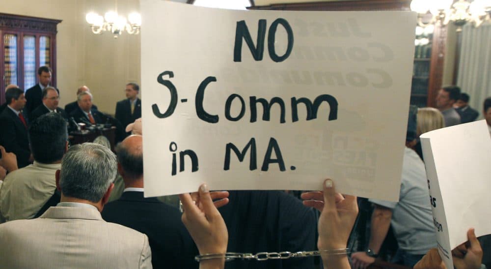 In this file photo, protesters wearing handcuffs holds up signs urging the stop of the "Secure Communities" program, or "S Comm," at a news conference held by Massachusetts county sheriffs at the Statehouse in Boston, Wednesday, Sept. 28, 2011. (Charles Krupa/AP)