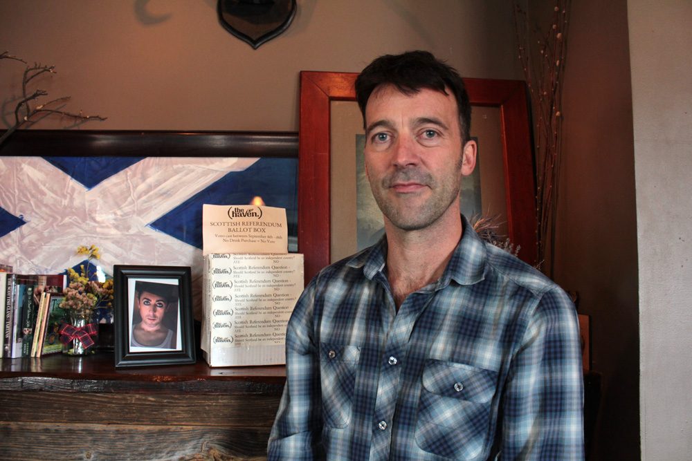 The owner of the Haven, Scotsman Jason Waddleton, in front of the pub's "ballot box" (Shannon Dooling/WBUR)
