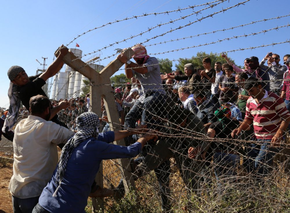 In this Friday, Sept. 26, 2014 photo, Kurds from Turkey, right, and Syria break down the barbed wire at the Turkey-Syria border near Suruc, Turkey. Turkish President Recep Tayyip Erdogan said Friday that a "no-fly zone" should be created in Syria to protect part of it from attacks by Syria's air force. In his comments to reporters on his return from the U.N. General Assembly in New York, Erdogan did not specify where such a zone should be located. (AP)