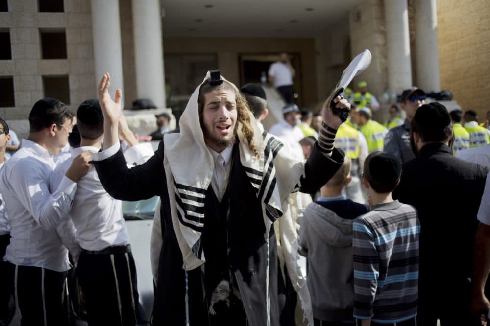 An ultra-Orthodox Jewish man prays as Israeli rescue workers clean the scene of a shooting attack in a Synagogue in Jerusalem. (Ariel Schalit/AP)