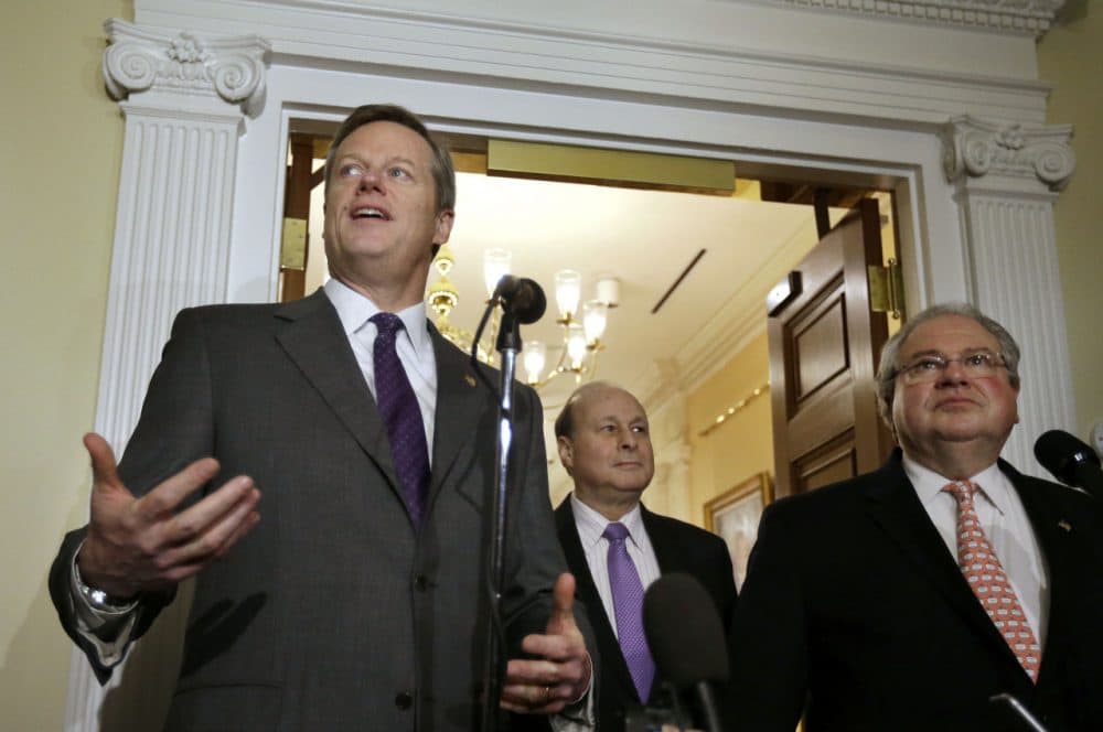 Gov. Charlie Baker speaks to reporters as Senate President Stanley Rosenberg, center, and House Speaker Robert DeLeo look on during a news conference Monday outside the governor's office. The trio are facing a state budget gap. (Steven Senne/AP)