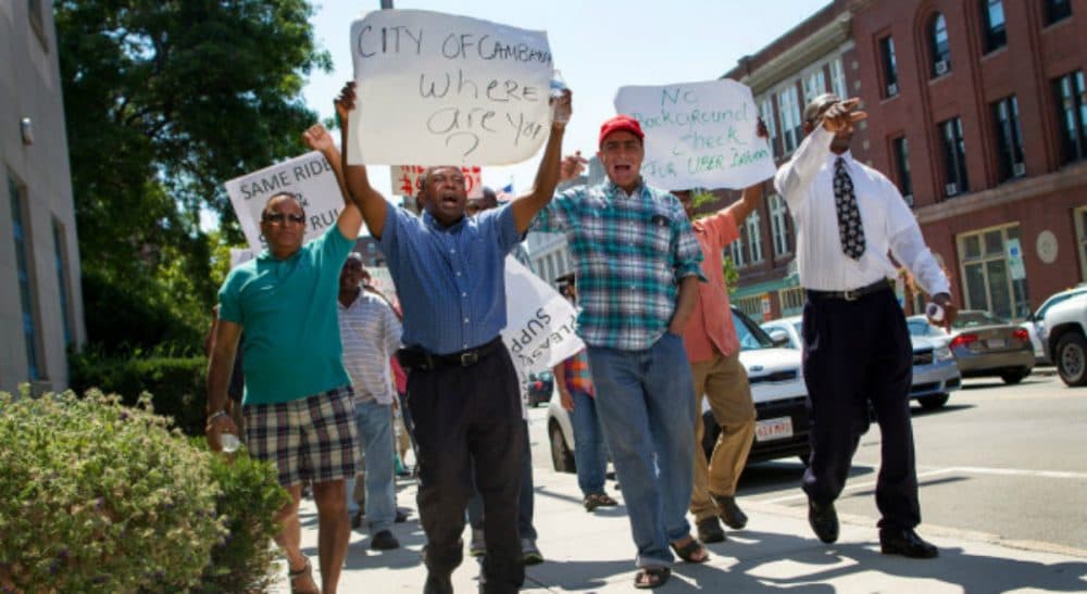 Tom LeCompte: "The 'one-day' strike in front of City Hall barely lasted a half-day, breaking up in time for drivers to catch the rush hour business to Logan or the hotels." Pictured: Cambridge taxi drivers protest on the street outside City Hall Monday, August 3, 2015. (Hadley Green/WBUR)