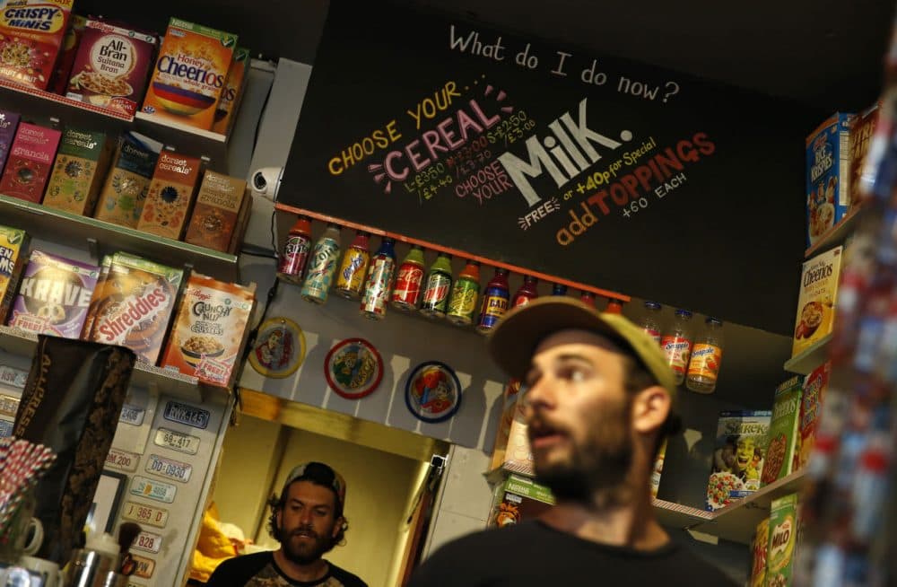 A member of staff of the Cereal Killer Cafe helps point out to a customer the range of cereals available, from U.S. favorites to European gluten free organics, at the cafe in Brick Lane, London, Wednesday, Sept. 30, 2015. The Cereal Killer Cafe has drawn both derision and big crowds since it opened nine months ago, offering a cornucopia of flakes, pops and puffs from about 3 pounds ($4.50) a bowl. Now it has attracted the ire of anti-gentrification protesters, who last week surrounded the business with flaming torches and scrawled "scum" on its windows as customers sheltered in the basement. (Alastair Grant/AP)