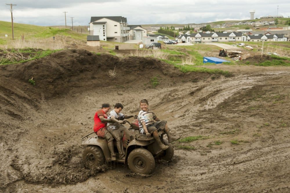 Children ride an ATV through a muddy construction area at the edge of a housing development in Watford City, North Dakota, one of many built during the oil boom. (Andrew Cullen)