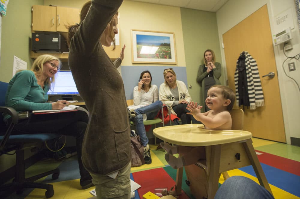 James smiles and claps as occupational therapist Victoria Peake tests his development during a check up at the Newborn Developmental Follow up Clinic at Massachusetts General Hospital. Director of the Clinic, Dr. Leslie Kerzner is seated left and James' adoptive mother Kristen Fountaine in the center. (Jesse Costa/WBUR)