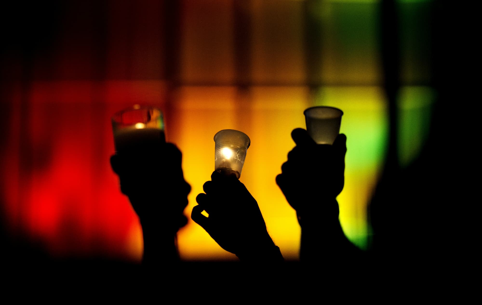People hold up candles against a rainbow lit backdrop during a vigil for those killed in a mass shooting at the Pulse nightclub, Monday, June 13, 2016, in Orlando, Fla. (David Goldman/AP)