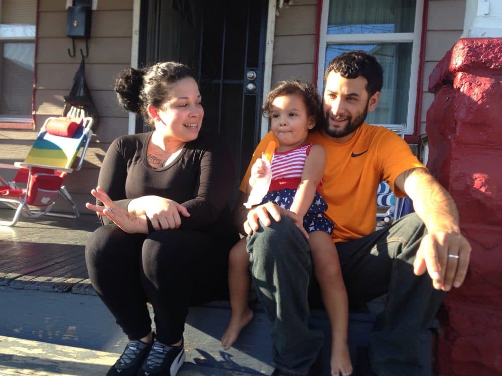 Cinthia Cruz (left) and her boyfriend Juan Rivera sit on their front steps with their daughter Zahira. Cruz and Rivera live in Cleveland, and make $1,400 a month to support their family. (Peter O'Dowd/Here & Now)
