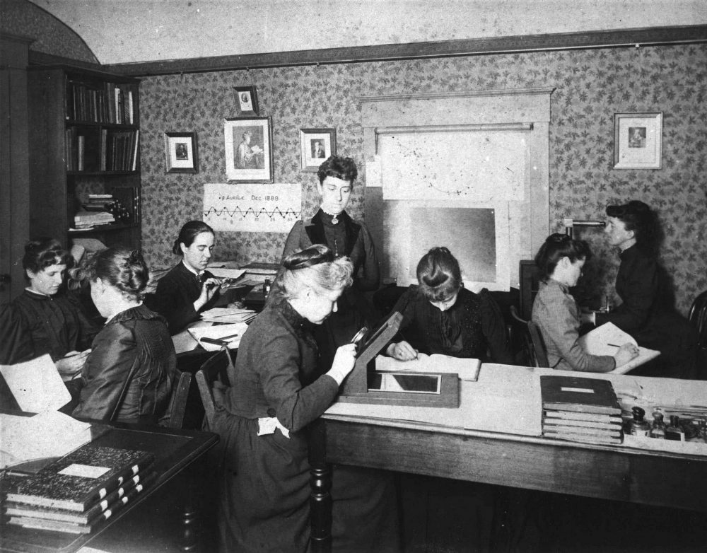 Harvard Computers at work, circa 1890, including Henrietta Swan Leavitt seated, third from left, with magnifying glass (1868–1921), Annie Jump Cannon (1863–1941), Williamina Fleming standing, at center (1857–1911), and Antonia Maury (1866–1952) c. 1890. (Harvard College Observatory)