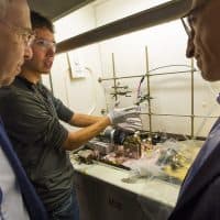 Harvard graduate student Andrew Wong, center, demonstrates his lab prototype of an organic mega flow battery to professor Roy Gordon, left, and professor Michael Aziz. (Jesse Costa/WBUR)
