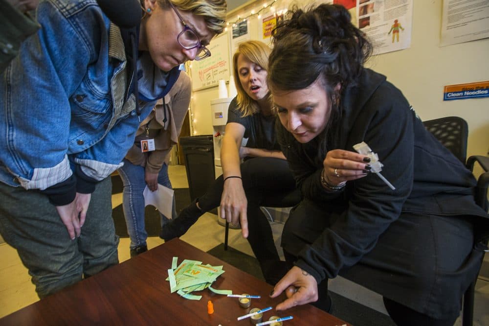 Jess Tilley, right, gives a demonstration with her fentanyl test strips. At left is needle exchange worker Emily Moulton and in the center is Liz Whynott, Tapestry Health's director of HIV health and prevention. (Jesse Costa/WBUR)