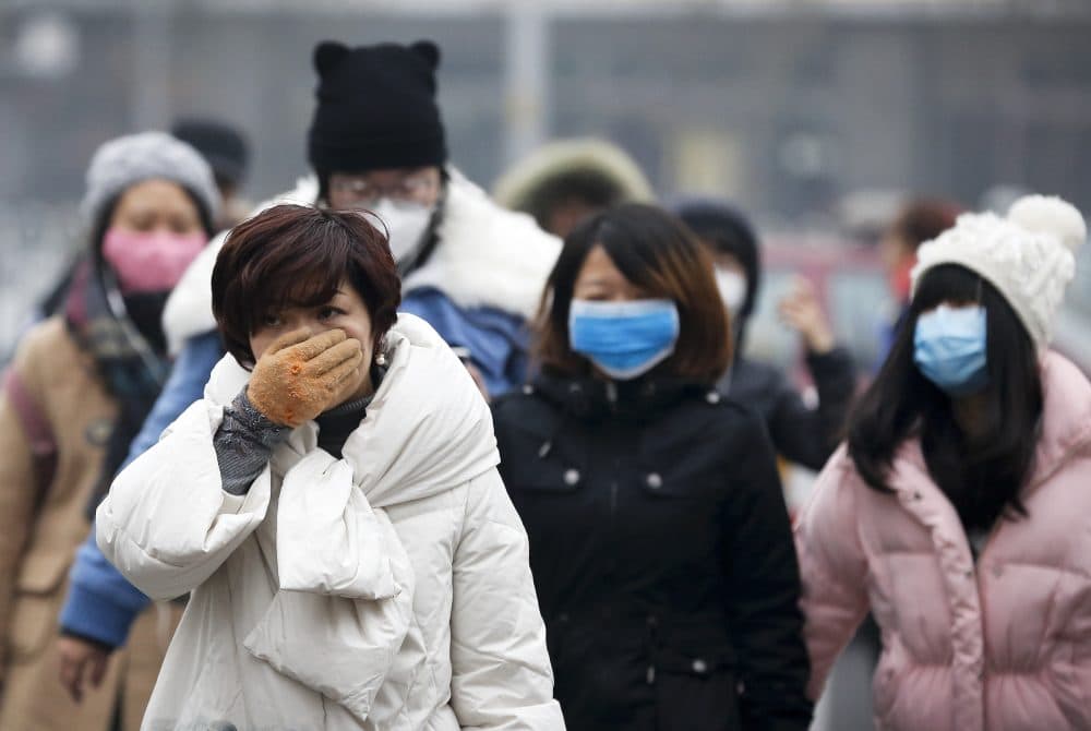 A woman uses her hand to cover her face from pollutants as people walk along a street on a polluted day in Beijing, Tuesday, Dec. 8, 2015. (Andy Wong/AP)