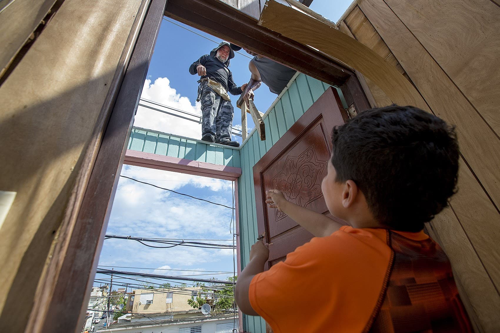 Jose Lopez hands a small board to Anthony Geigel and Israel Garcia to repair their roof in Barrio Obrero Santurce. (Jesse Costa/WBUR)