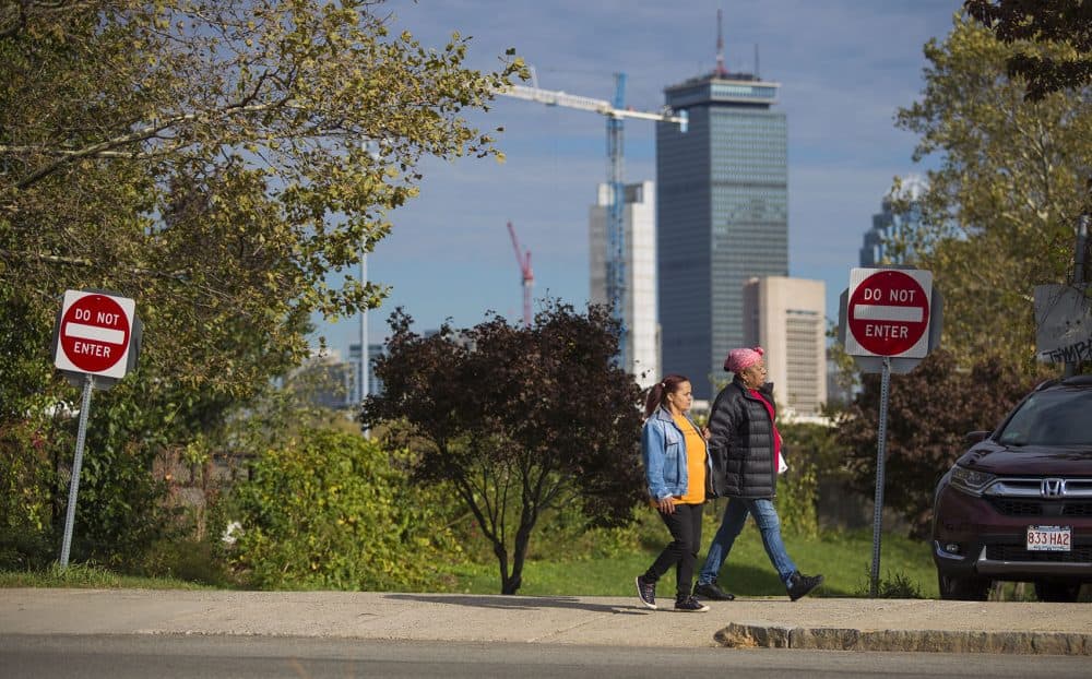 Two women walk down the street along Malcolm X Boulevard in Roxbury, with downtown Boston in the background. (Jesse Costa/WBUR)