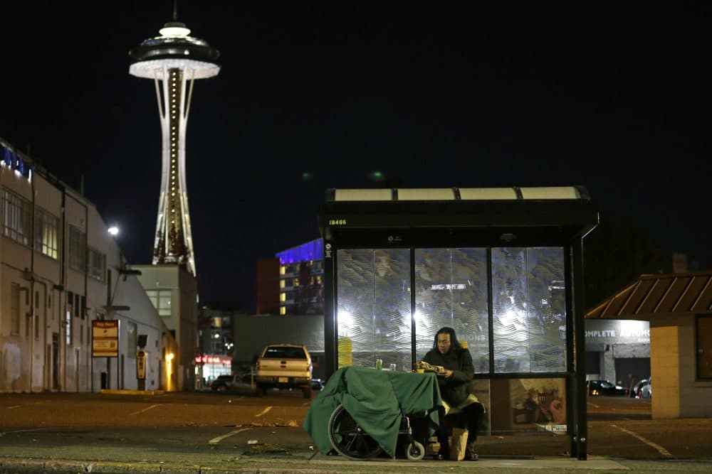 In this Oct. 30, 2017 photo, Dave Chung, who says he has been homeless for five years on the streets of California and Washington state, eats a meal before bedding down in a bus shelter in view of the Space Needle in Seattle. Chung says he has been offered shelter many times, but chooses to remain outside due to the living conditions in homeless shelters and conflicts he has with other people. (Ted S. Warren/AP)