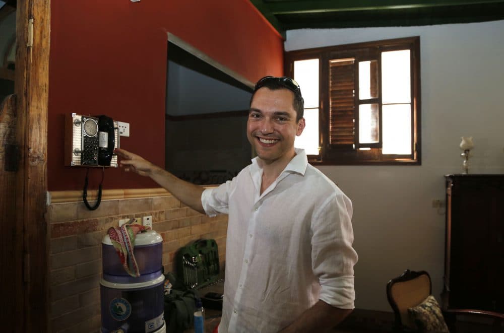 In this file photo from June 2015, co-founder of AirBnb Nathan Blecharczyk smiles to the camera as he points to an old telephone inside the guesthouse of Armando Usain in Havana, Cuba. (AP Photo/Desmond Boylan)