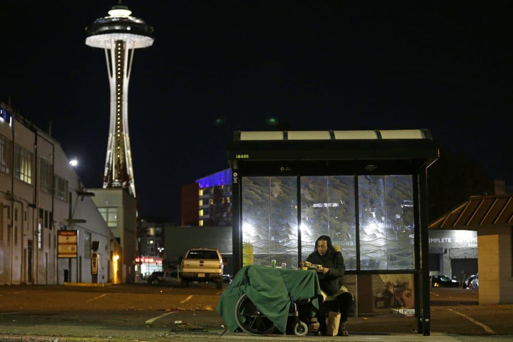 In this Oct. 30, 2017 photo, Dave Chung, who says he has been homeless for five years on the streets of California and Washington state, eats a meal before bedding down in a bus shelter in view of the Space Needle in Seattle. Chung says he has been offered shelter many times, but chooses to remain outside due to the living conditions in homeless shelters and conflicts he has with other people. (AP Photo/Ted S. Warren)