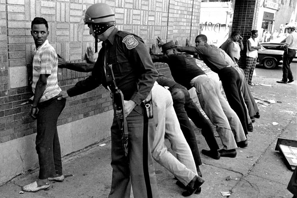 FILE - In this July 24, 1967 file photo, a Michigan State police officer searches a youth on Detroit's 12th Street where looting was still in progress after the previous day's rioting. The last surviving member of the Kerner Commission says he remains haunted that the panel's recommendations on US race relation and poverty were never adopted, but he is hopeful they will be one day. Former U.S. Sen. Fred Harris says 50 years after working on a report to examine the causes of the late 1960s race riots he strongly feels that poverty and structural racism still enflames racial tensions even as the United States becomes more diverse. (AP Photo/File)