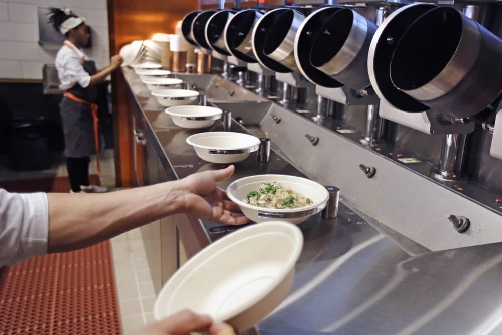 A worker lifts a lunch bowl off the production line at Spyce, a restaurant which uses a robotic cooking process, in Boston, Thursday, May 3, 2018. Robots can't yet bake a souffle or fold a burrito, but the new restaurant in Boston is employing what it calls a "never-before-seen robotic kitchen" to cook up ingredients and spout them into a bowl. (Charles Krupa/AP)