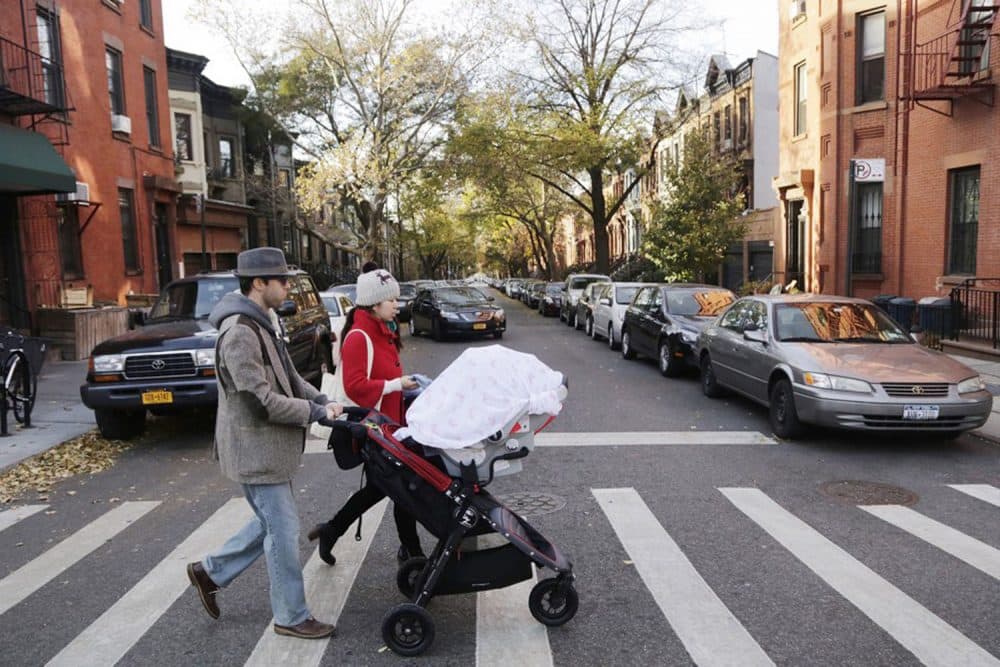 FILE - In this Nov. 14, 2013 file photo, a couple with a baby stroller cross the street in the Park Slope neighborhood in the Brooklyn borough of New  York. The rise in popularity of Brooklyn as a name for girls parallels the borough’s renaissance through the gentrification of neighborhoods, an influx of tech firms, the construction of the Barclays Center as an entertainment hub and the relocation and rebranding of the New Jersey Nets basketball team. (AP Photo/Mark Lennihan, FILE)