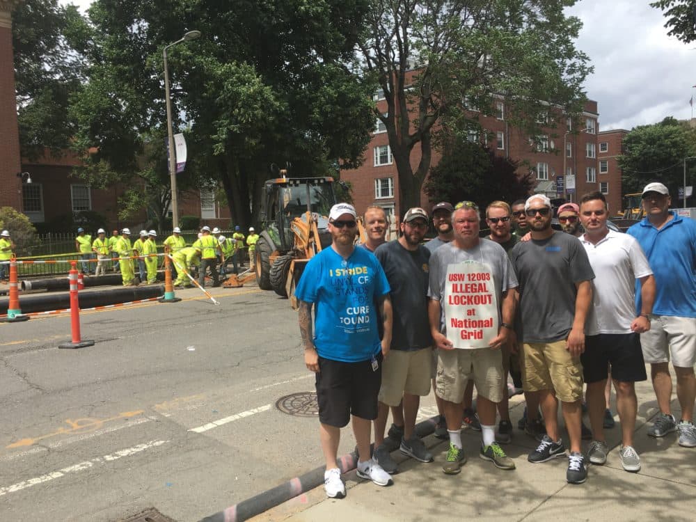 Unionized National Grid employees protest near Boston's Longwood Medical Area with replacement workers in the background. Workers were called in after a gas line was damaged during waterline repair. (Bruce Gellerman/WBUR)
